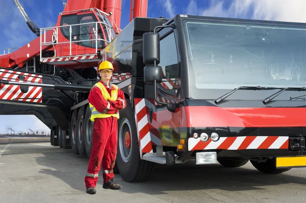 Worker in red uniform and hard hat standing by large mobile crane