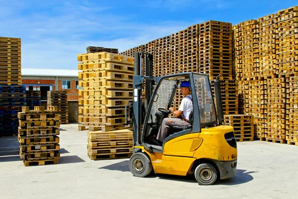 man operating yellow forklift near stacked wooden pallets
